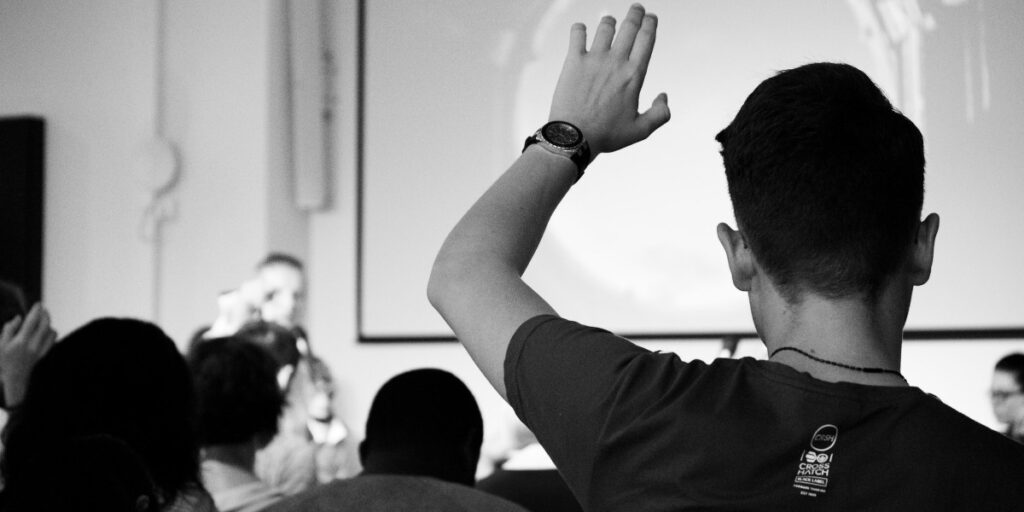 Photo en noir et blanc d'un étudiant qui lève la main dans un auditorium universitaire.
