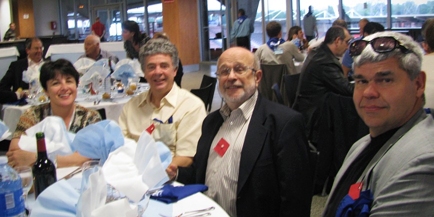 Une femme et trois hommes sont attablés à une table ronde. Ils portent un carré rouge à la boutonnière.