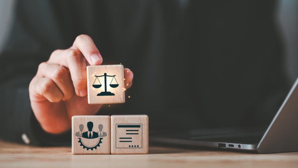 Une main sur fond noir tient une tuile de bois représentant la balance de la justice.